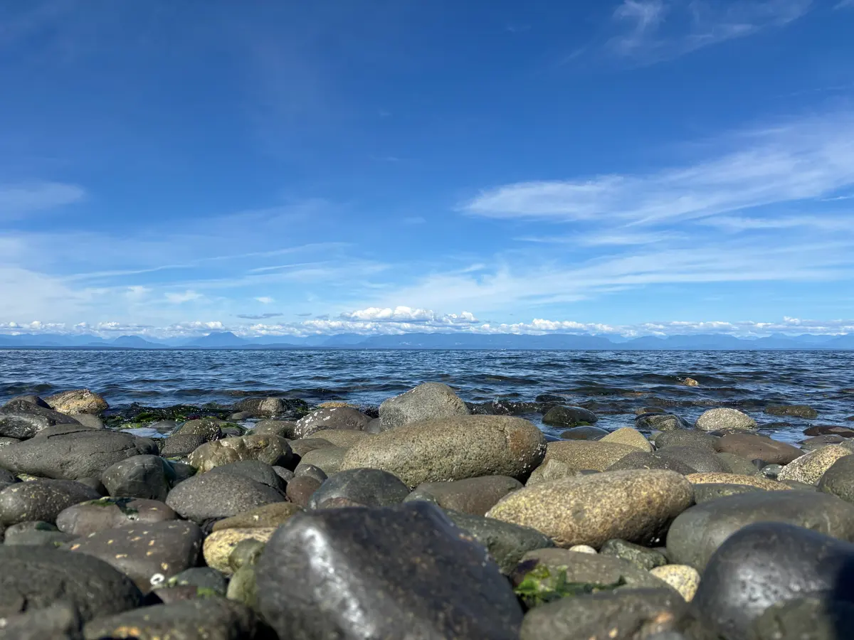 Smooth beach stones in the foreground and snow-capped mountains on the far shore