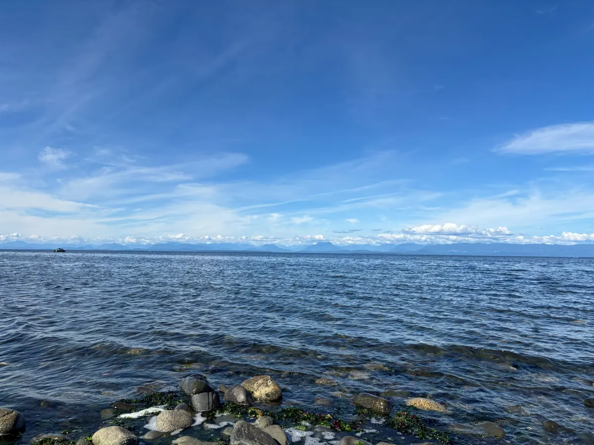 Calm water over a stony shore, with distant mountains and high thin cloud