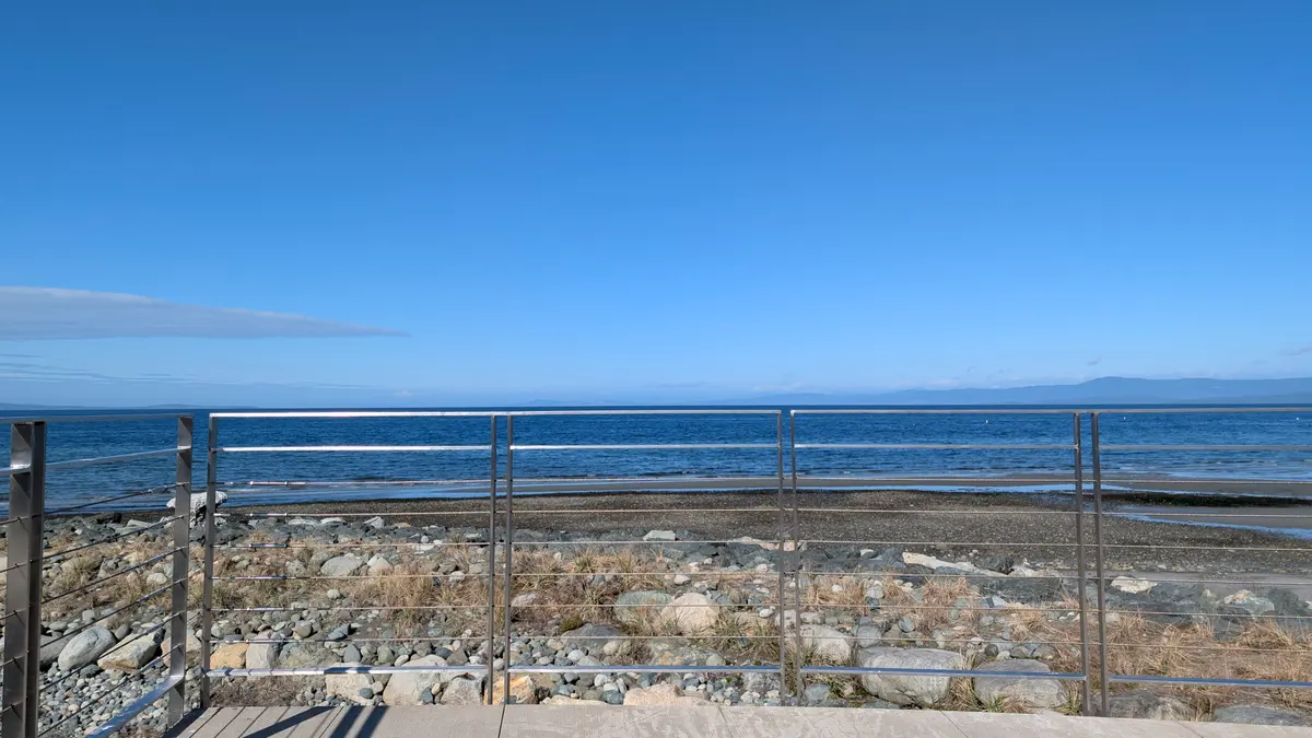 A steel railing above a stony beach on a clear blue day