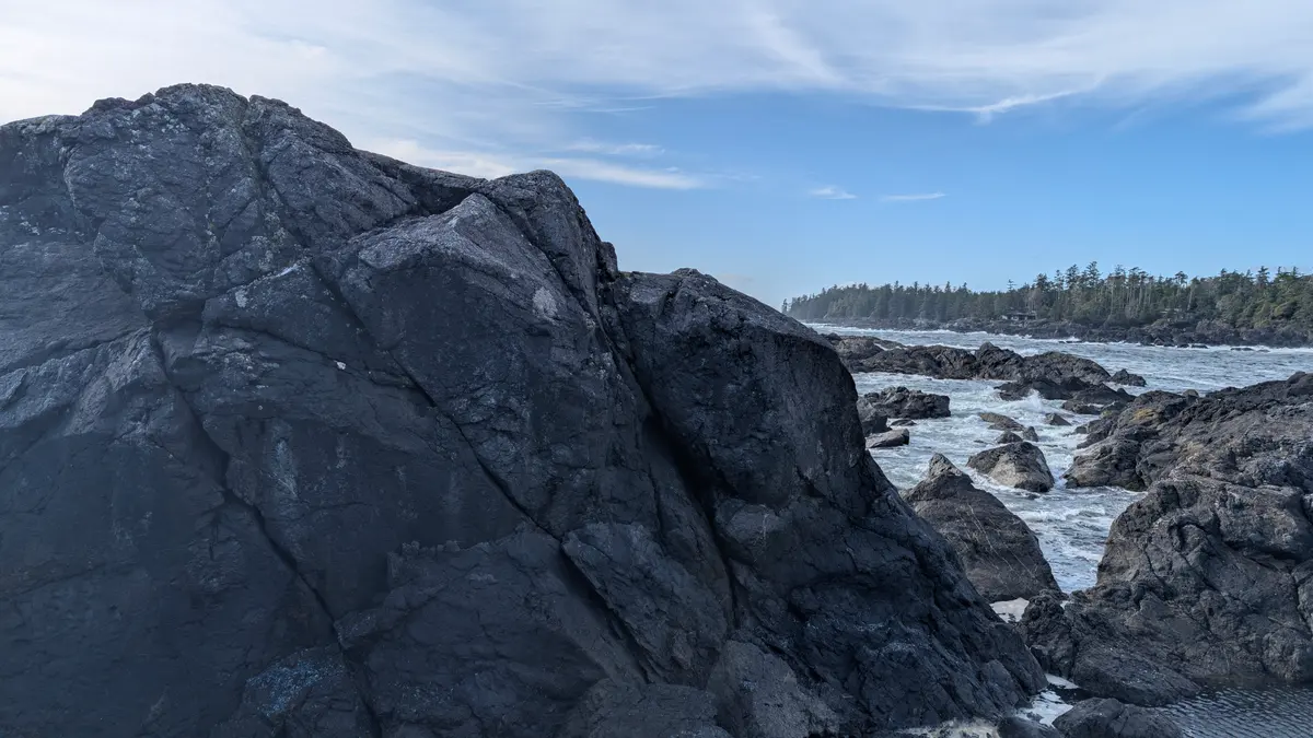 A large black rock face beside the surf on the Ucluelet coast